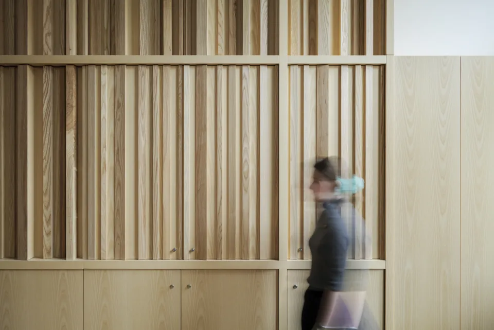 A woman walks past a wall with wood acoustic panelling